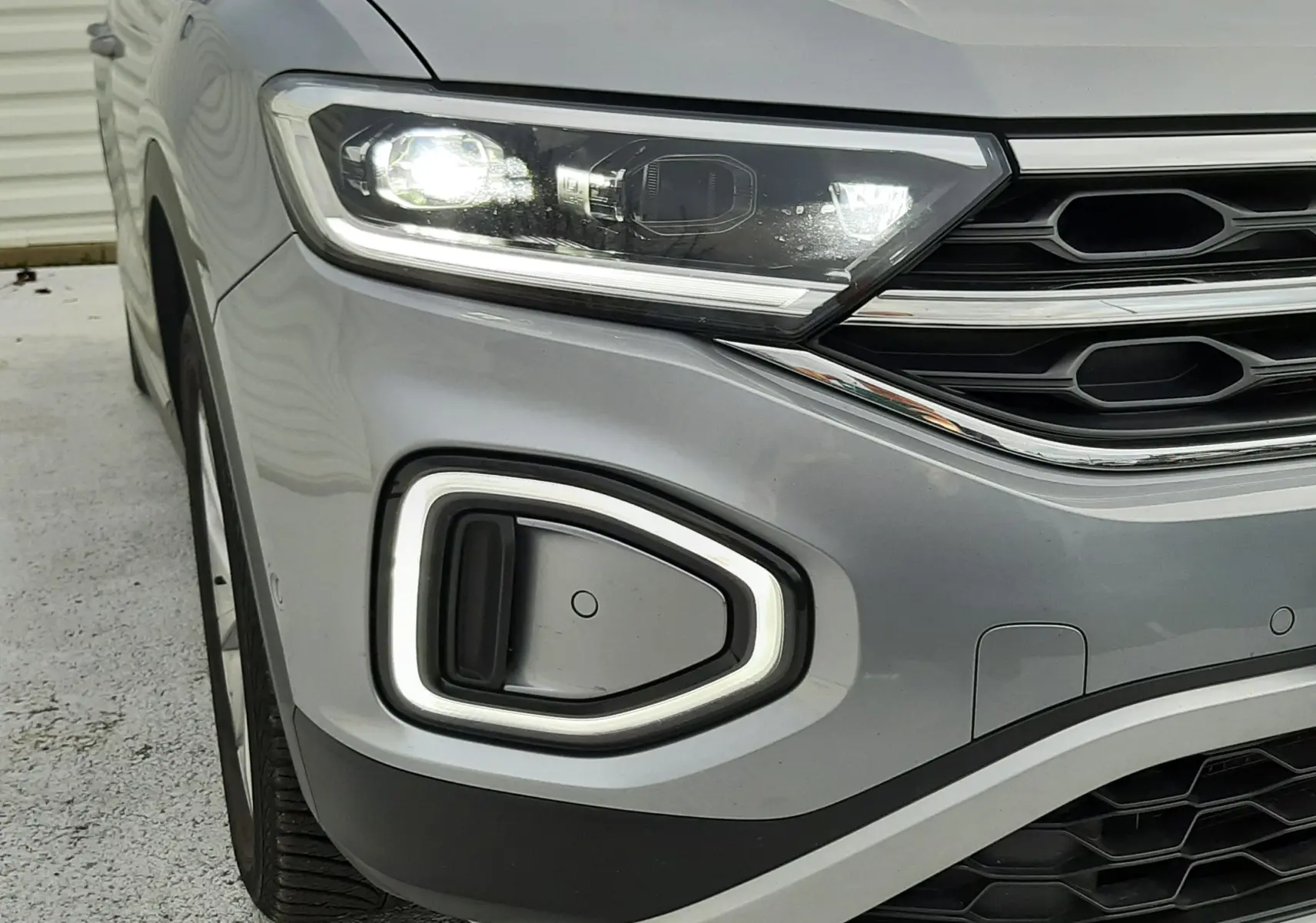Vue rapprochée en angle avant droit du Volkswagen T-Roc gris pyrite avec barres de toit argentées et vitres teintées.