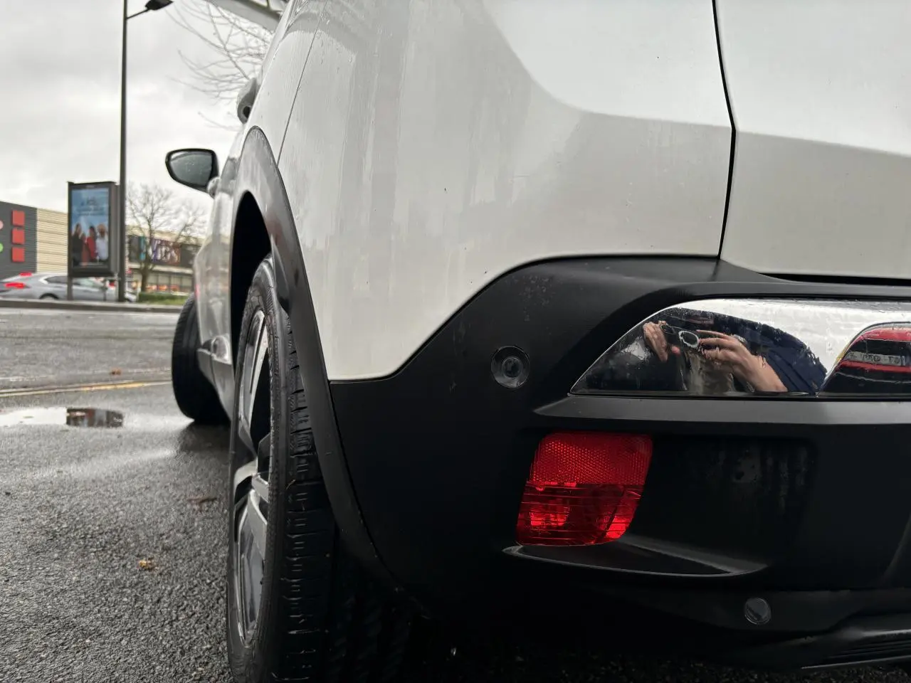 Vue arrière côté gauche d'un Peugeot 3008 blanc nacré avec feu arrière rouge et jante noire sur route humide.