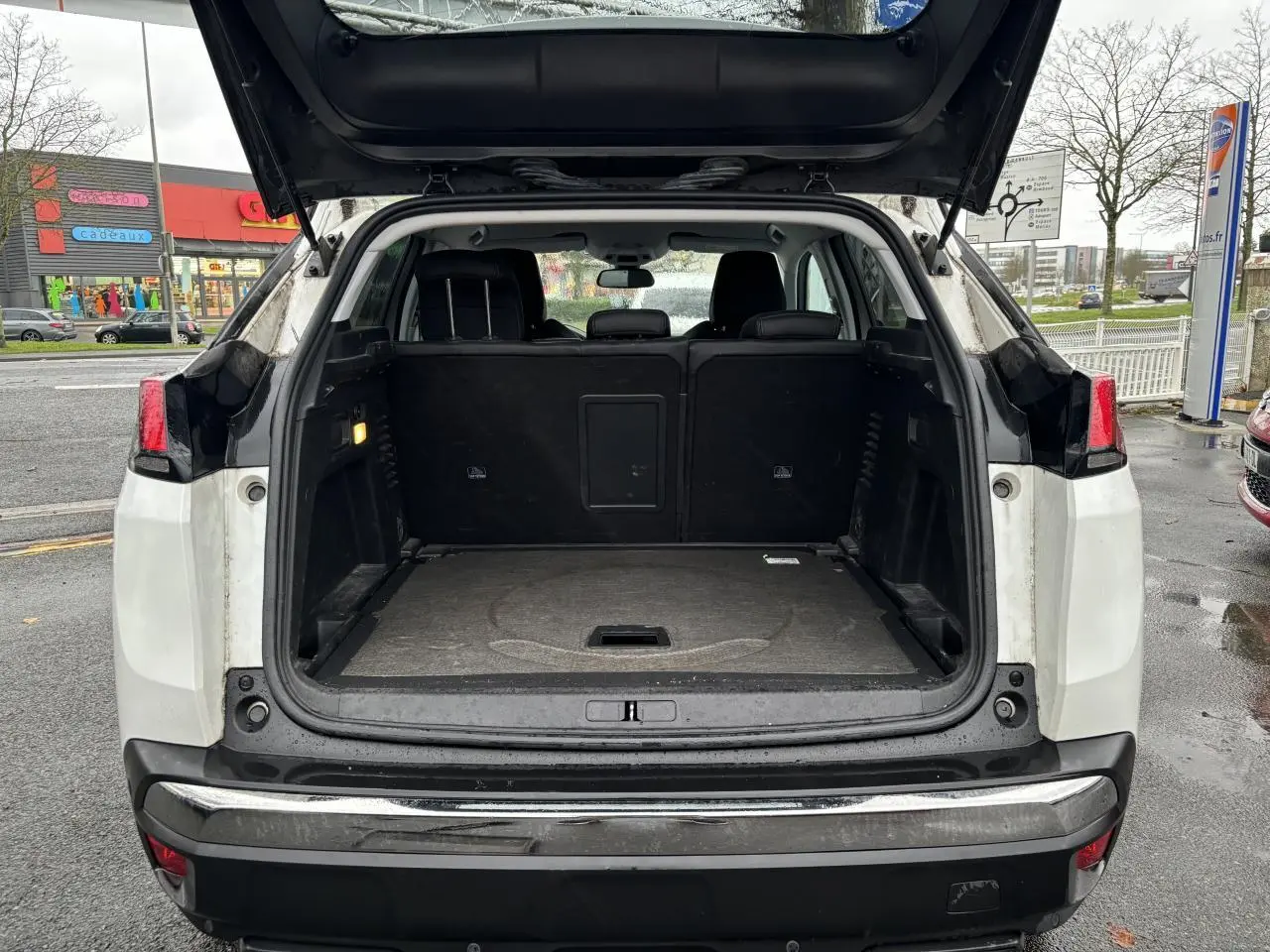 Coffre ouvert d'un Peugeot 3008 blanc nacré vu de l'arrière, montrant l'espace de chargement et les sièges arrière noirs.