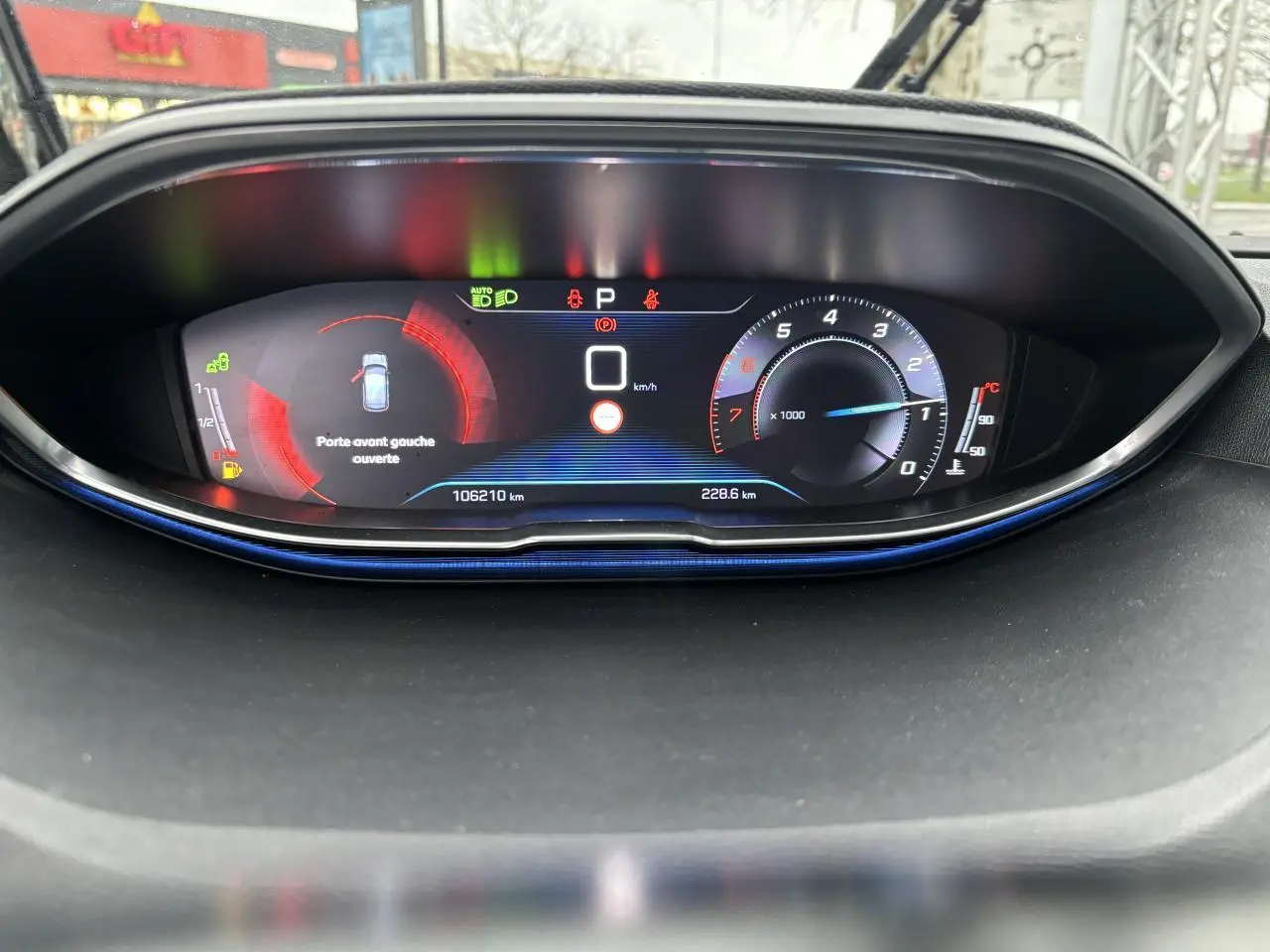 Tableau de bord numérique du Peugeot 3008 blanc, affichant la vitesse à zéro et porte avant gauche ouverte.