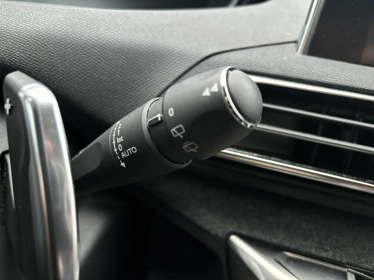 Gros plan sur la commande d’essuie-glace à gauche du volant dans l’habitacle du Peugeot 3008 blanc de 2018.