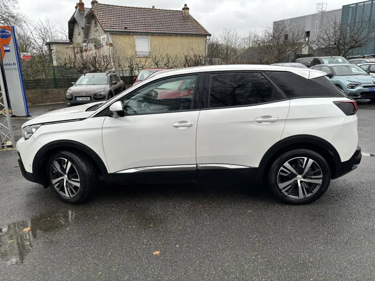 Profil côté gauche du Peugeot 3008 blanc nacré de 2018 avec toit noir et jantes alliage bicolores sur parking humide.