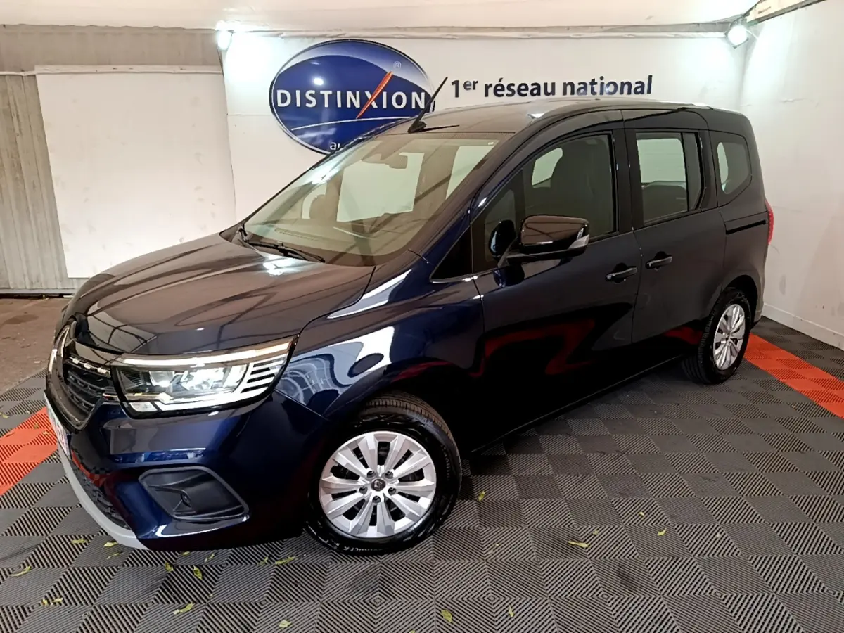 Renault Kangoo Equilibre TCe 100 bleu en 3/4 avant droit, avec phares LED et jantes alliage visibles en intérieur showroom.