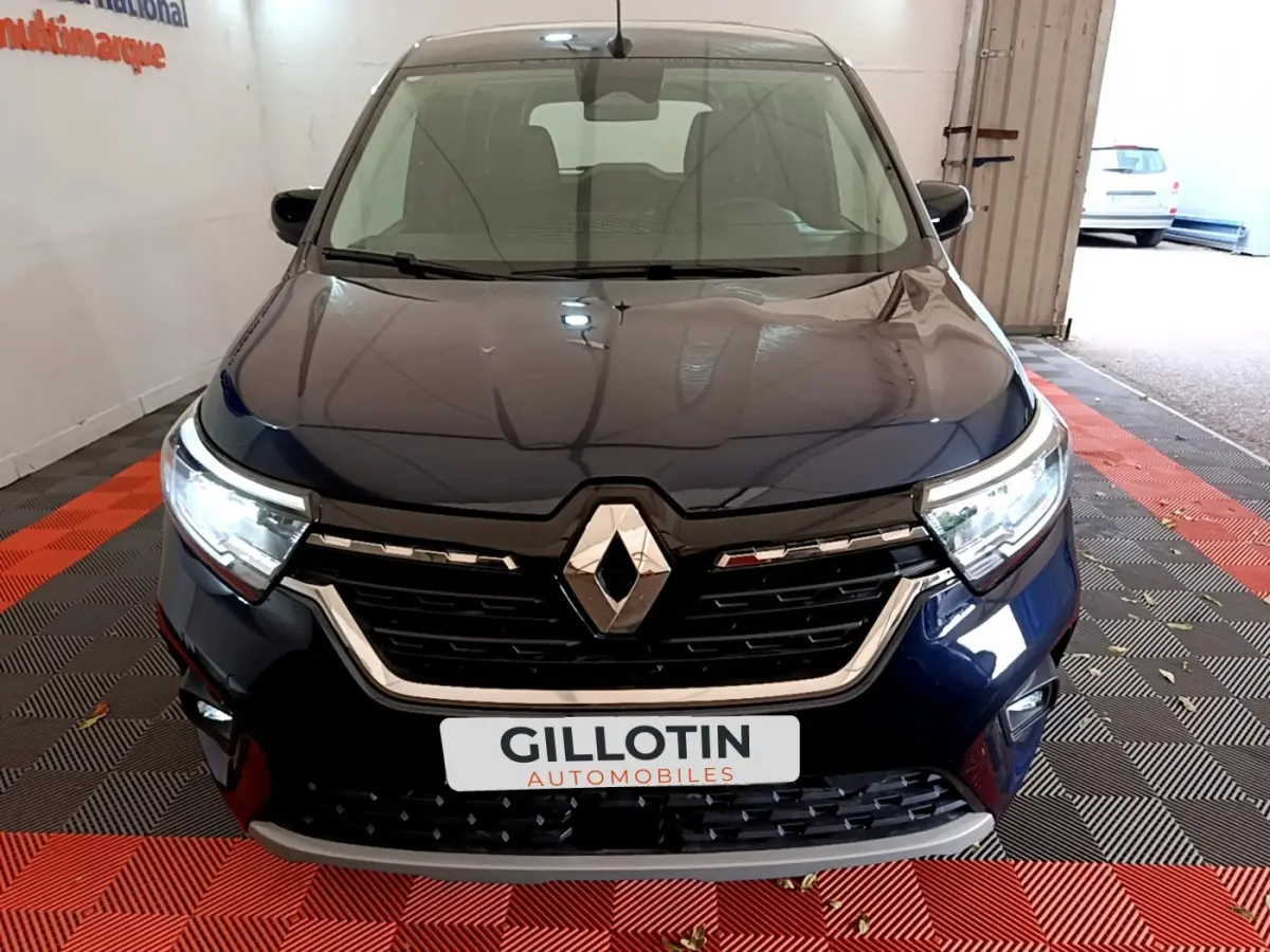 Vue frontale du Renault Kangoo Equilibre TCe 100 bleu 2023 avec calandre noire et phares LED allumés.