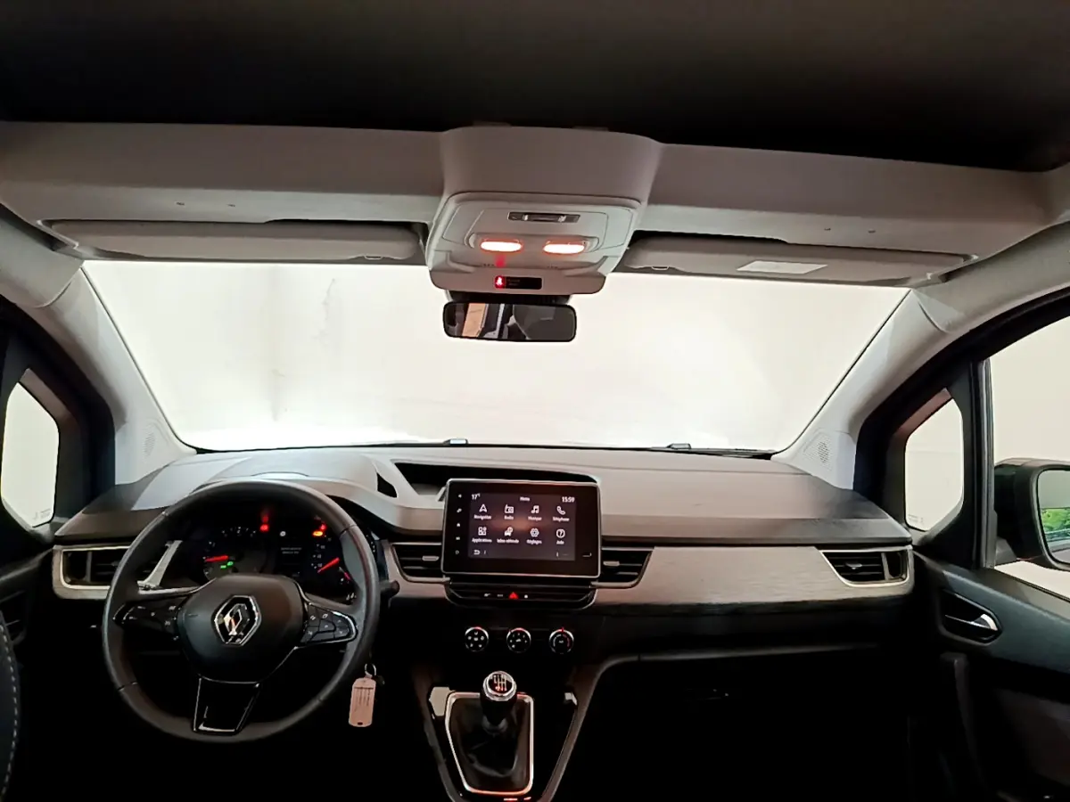 Vue intérieure avant du Renault Kangoo bleu 2023, tableau de bord moderne avec écran tactile central et volant multifonctions.