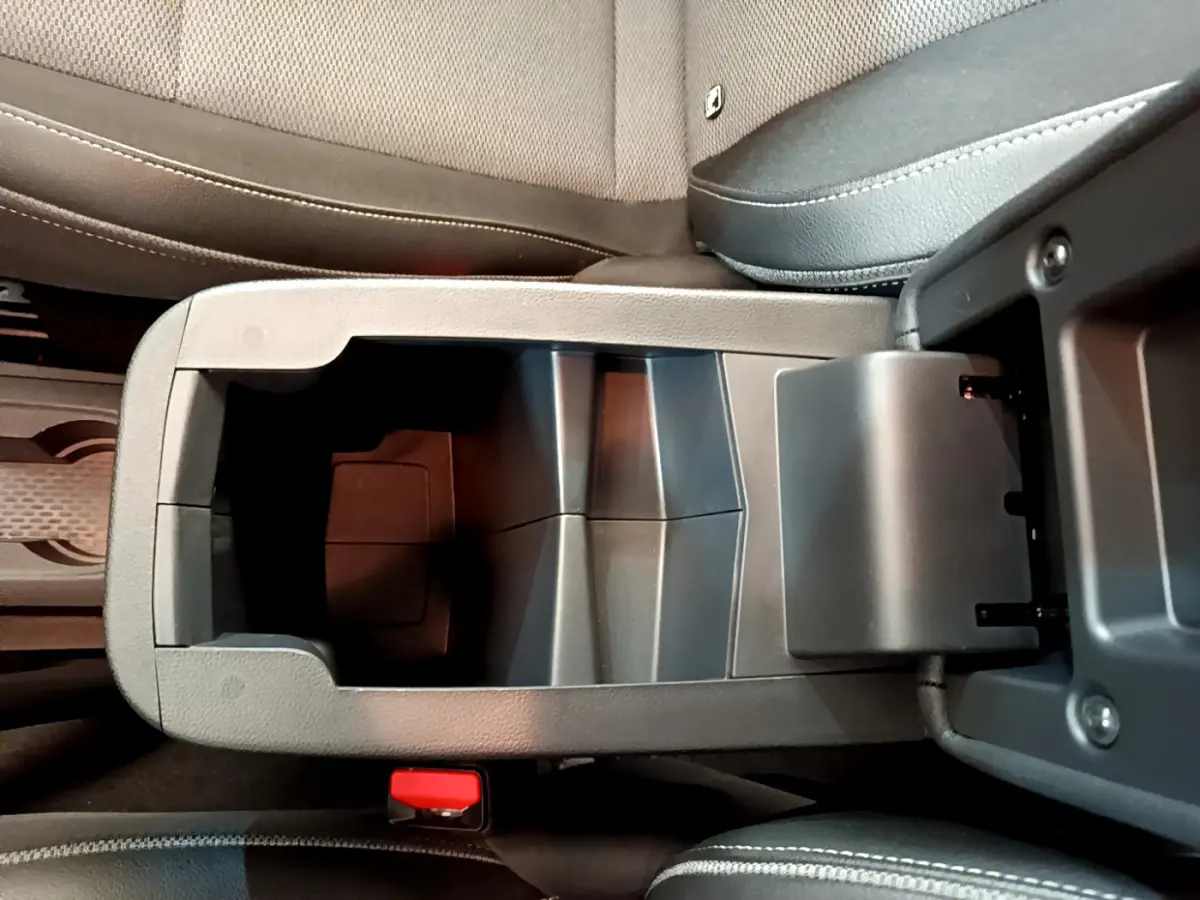 Vue rapprochée de la console centrale ouverte du Renault Kangoo 2023, sièges tissu gris visibles.