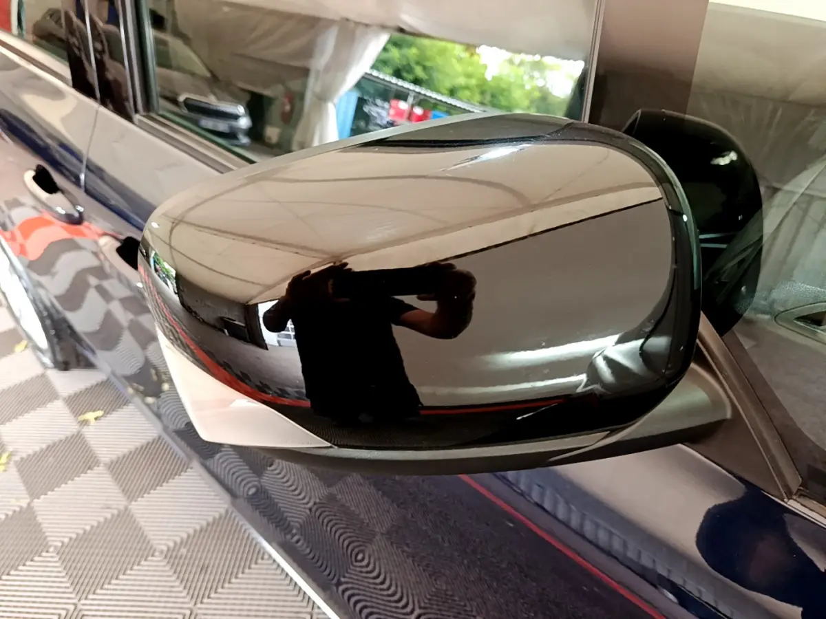 Rétroviseur droit noir brillant sur Renault Kangoo bleu, reflet de l'environnement intérieur du garage.