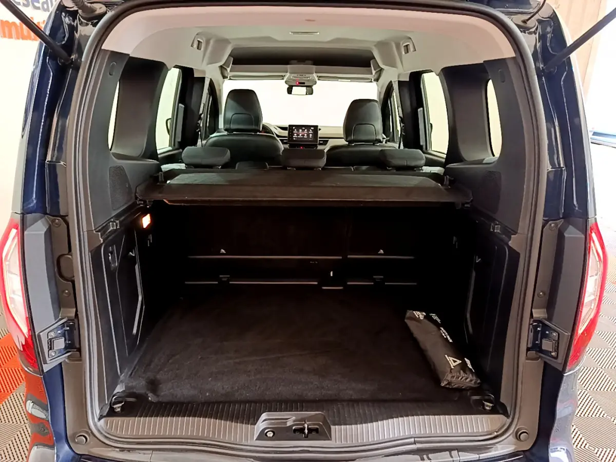 Vue arrière du coffre ouvert d'un Renault Kangoo bleu 2023, montrant l'intérieur spacieux et la tablette de séparation.