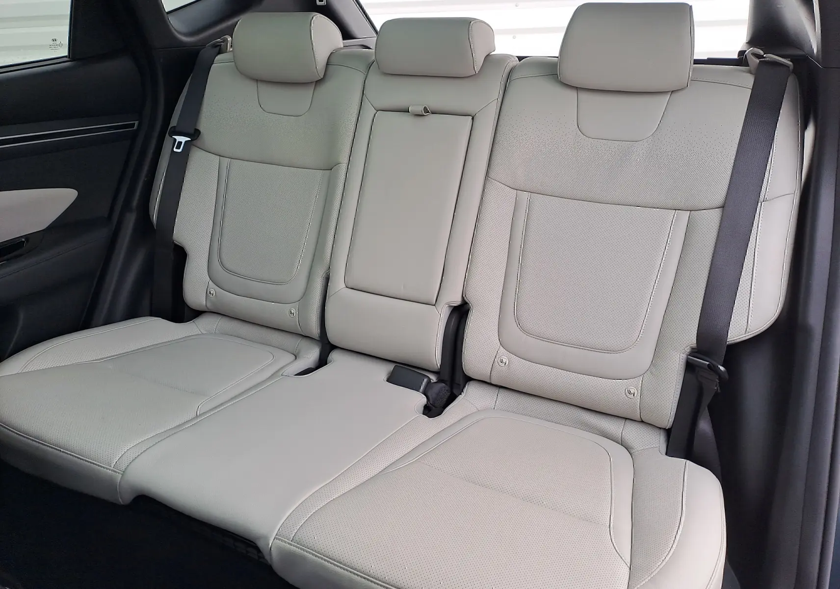 Vue intérieure des sièges arrière en cuir beige du Hyundai Tucson 2023, avec ceintures de sécurité visibles.