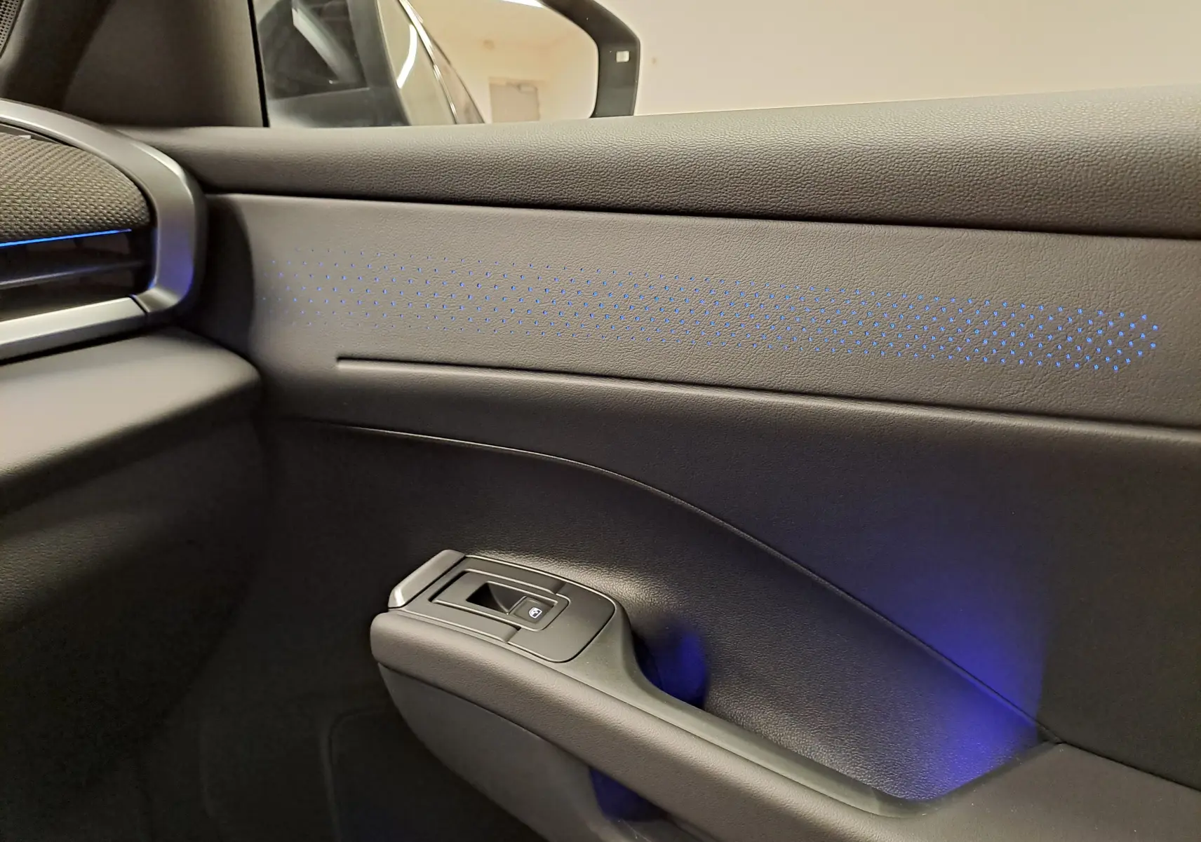 Détail de la porte côté droit du Volkswagen T-Roc 2026 noir ébène avec éclairage d'ambiance bleu subtil.