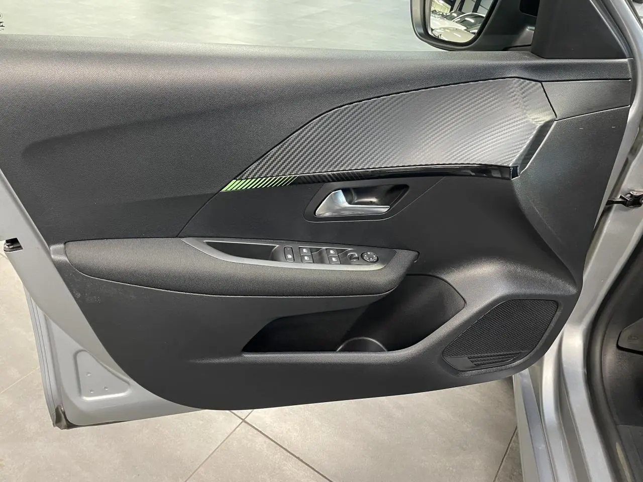 Vue rapprochée de la porte avant gauche gris clair du Peugeot 208 avec insert décor carbone et commandes électriques.