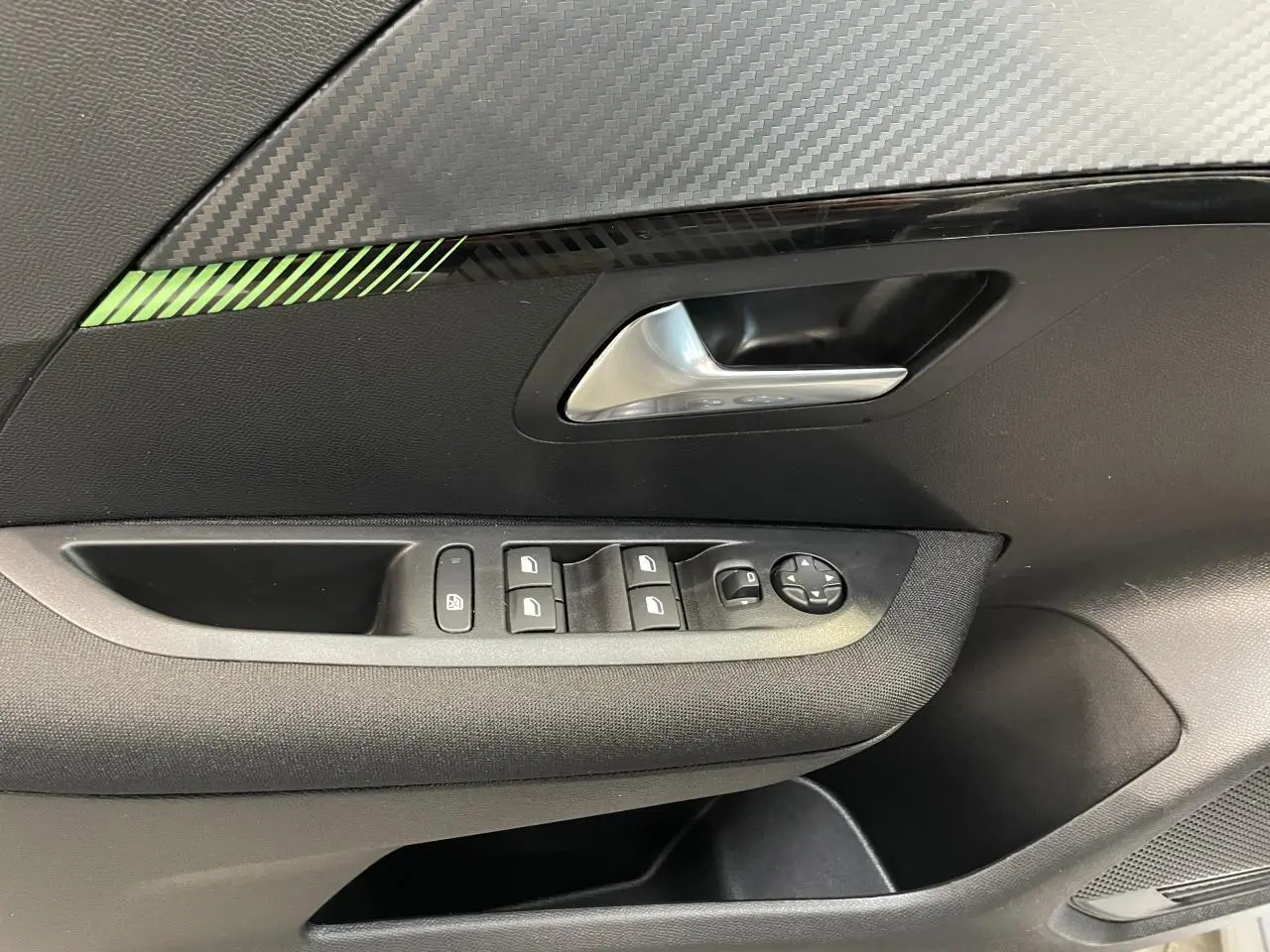 Détail de la porte avant gauche de la Peugeot 208 2024, avec commandes de vitres et décor carbone vert.