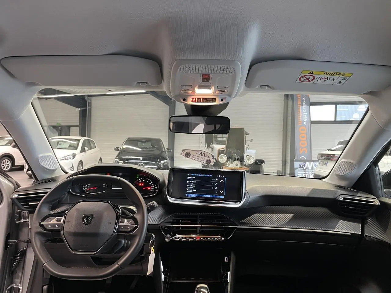 Vue intérieure avant du tableau de bord et volant noir de la Peugeot 208 1.2i PureTech 2024 avec écran tactile central.