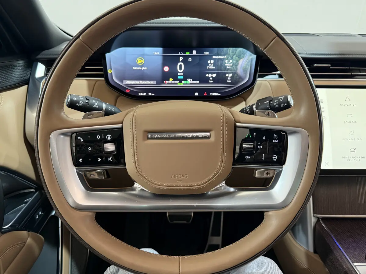 Vue rapprochée du volant cuir beige du Range Rover PHEV 2024 avec tableau de bord numérique et commandes intégrées.