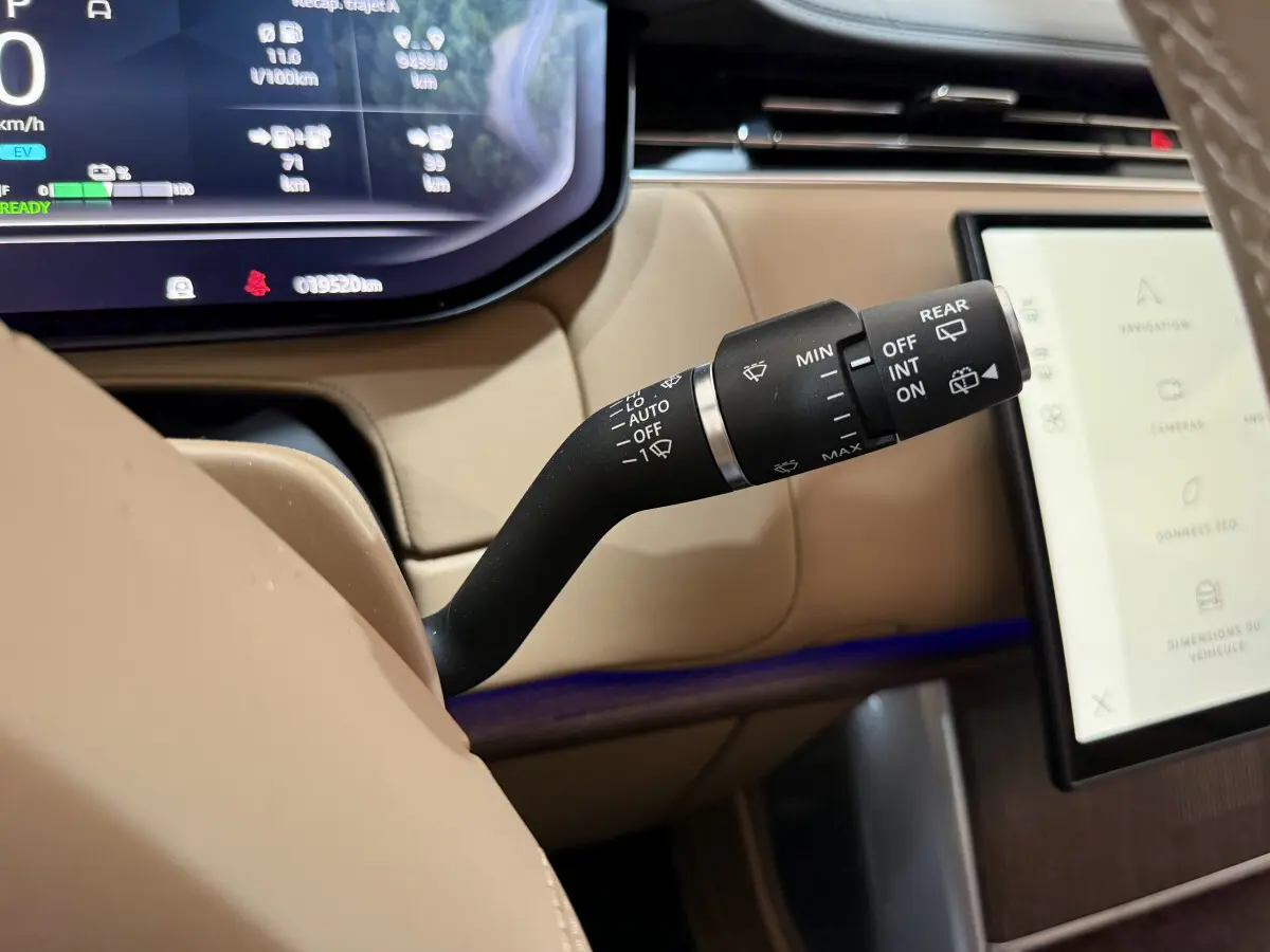 Gros plan sur la commande d’essuie-glace dans l’habitacle beige du Range Rover PHEV P550e noir, avec écran tactile visible.