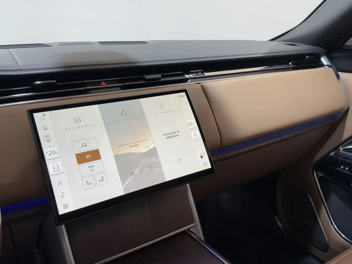 Vue intérieure du tableau de bord beige du Range Rover PHEV 2024 avec écran tactile central allumé.