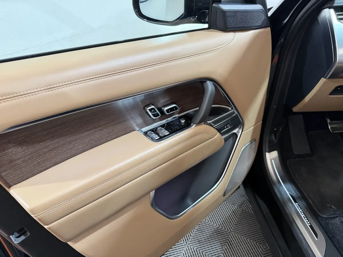 Vue intérieure côté gauche de la porte avant beige et bois du Range Rover PHEV 2024 avec commandes électriques et haut-parleur intégré.