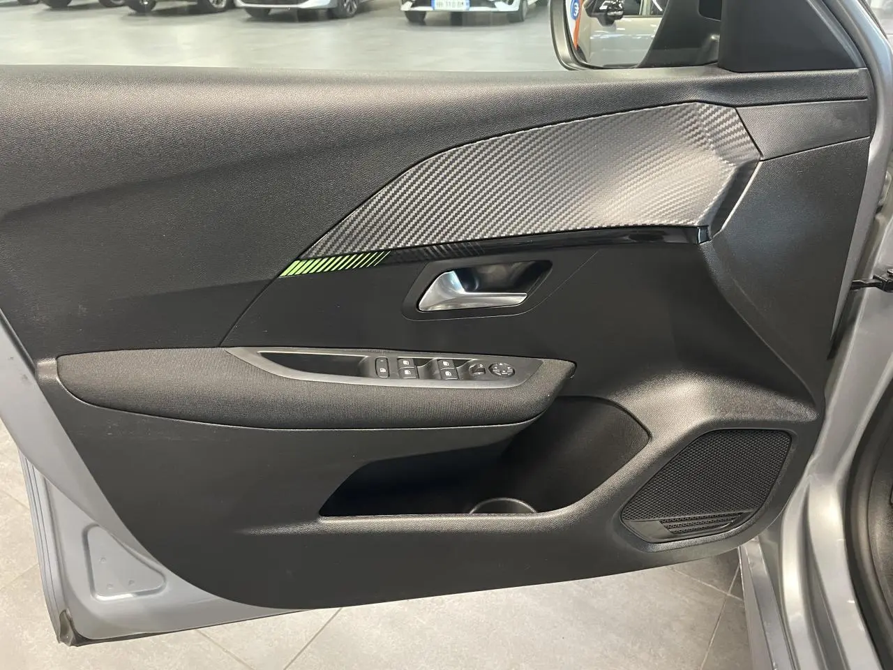 Vue intérieure de la porte avant gauche gris clair de la Peugeot 208 2024 avec insert carbone et commandes électriques.