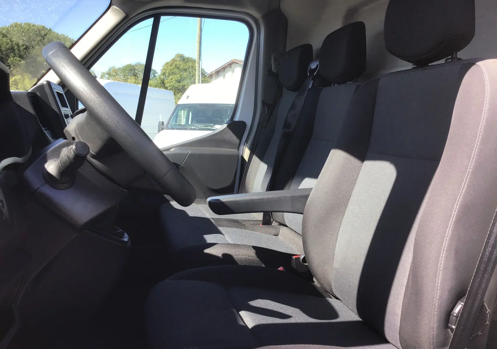 Vue intérieure côté conducteur du Renault Master blanc 2023, montrant les sièges noirs et le volant à gauche.