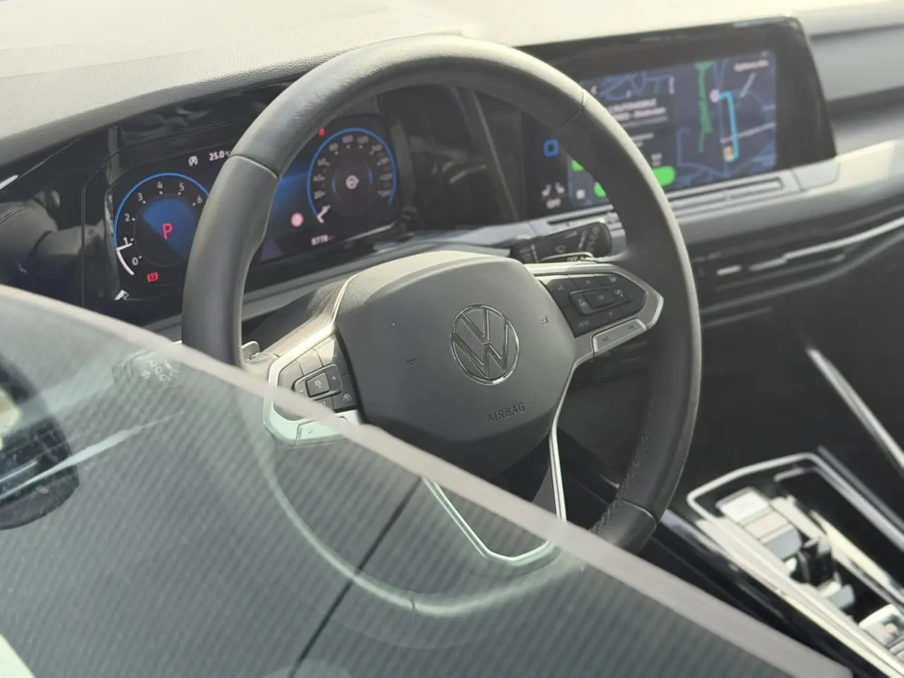 Vue intérieure centrée sur le volant multifonctions cuir de la Volkswagen Golf VIII 2024 avec tableau de bord numérique.
