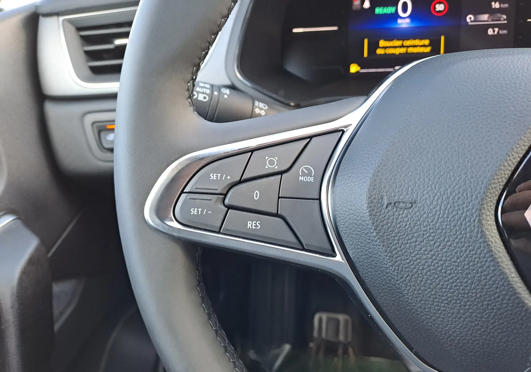 Gros plan sur les commandes gauche du volant du Renault Captur 2025, finition gris nacré avec affichage digital en arrière-plan.
