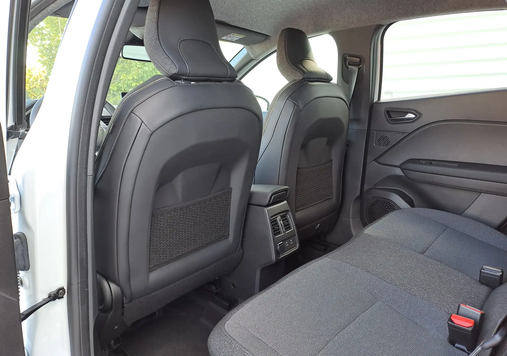 Vue arrière intérieure du Renault Captur 2025 blanc nacré, sièges avant en cuir noir et banquette tissu gris.