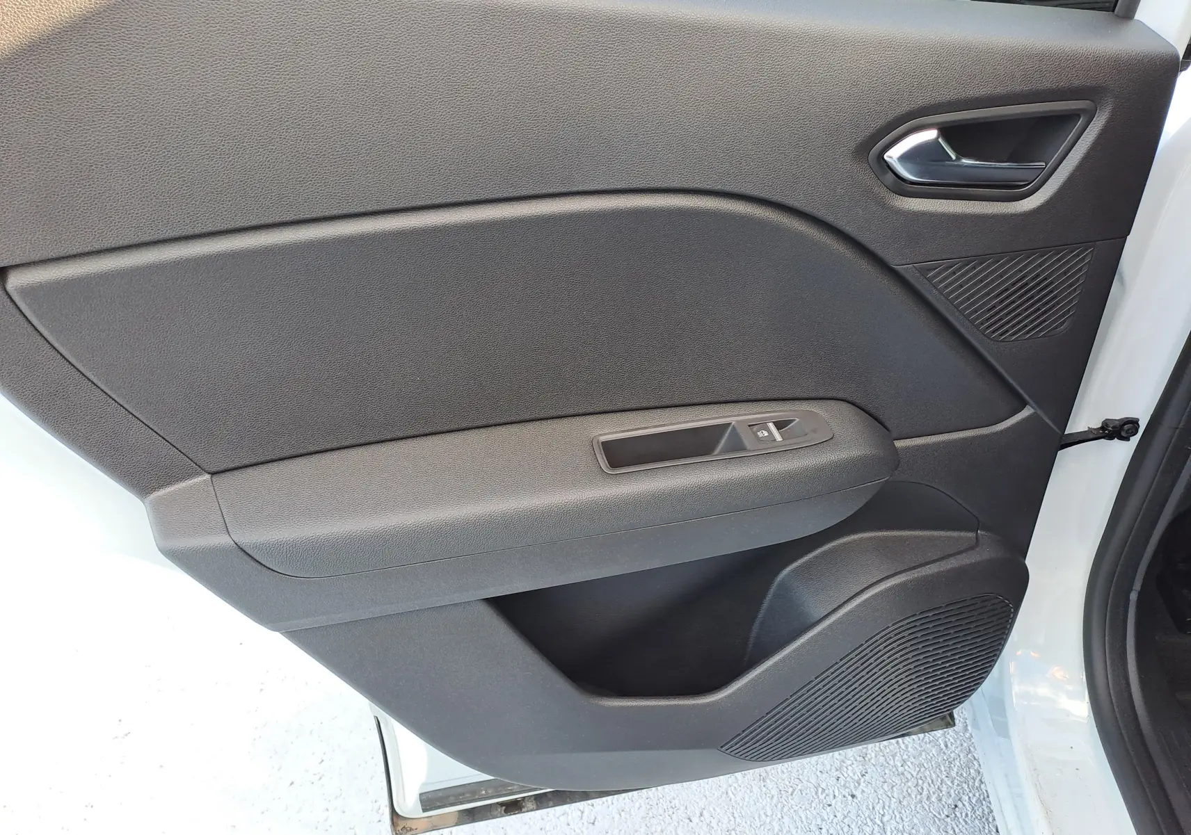 Gros plan sur la porte intérieure côté gauche du Renault Captur blanc nacré, avec commande de fenêtre et haut-parleur intégré.