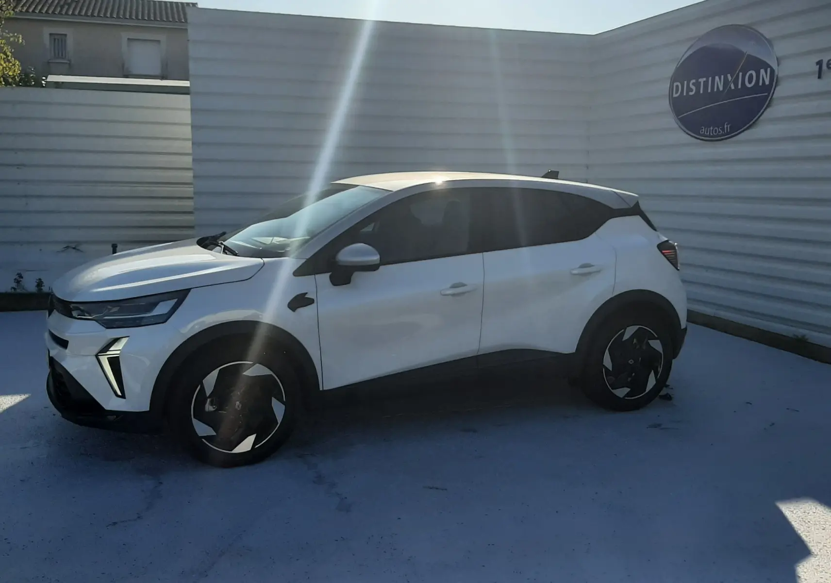 Renault Captur 2025 blanc nacré avec toit gris Highland vu de profil côté gauche, stationné devant un mur blanc.
