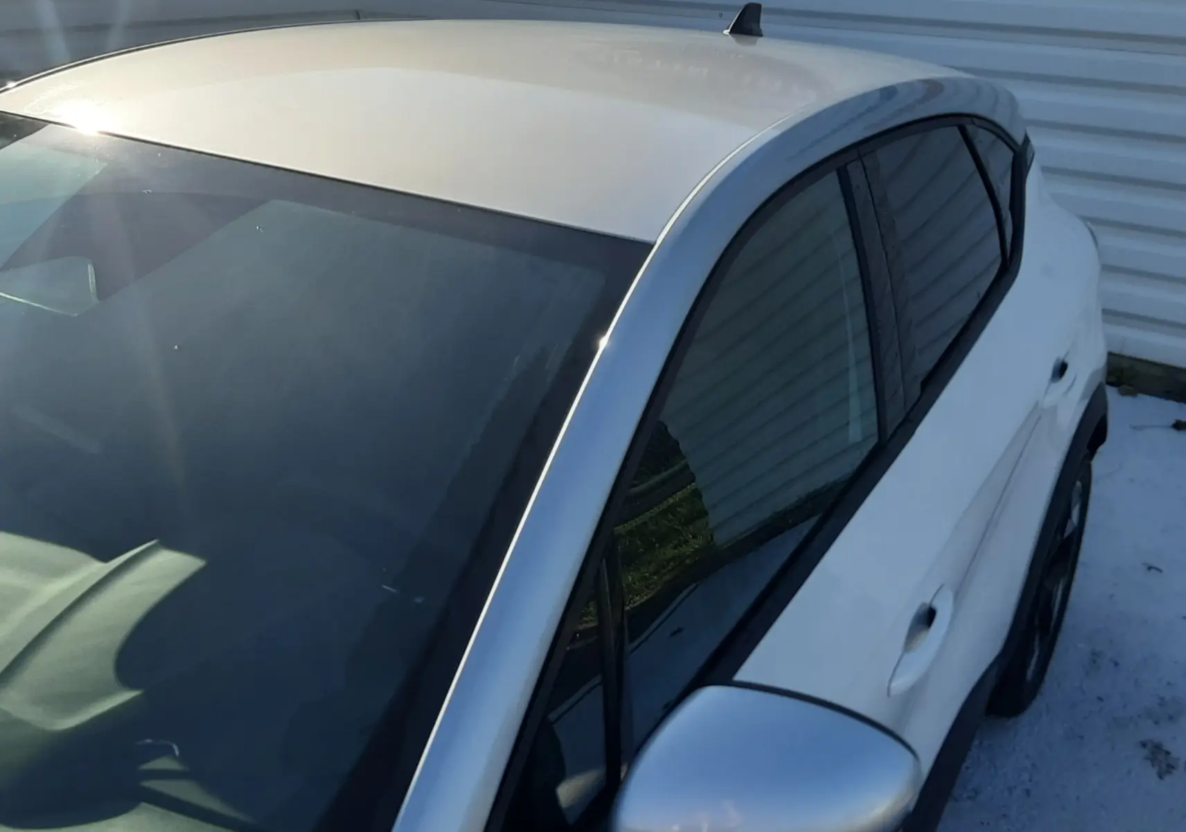 Vue 3/4 avant droit du Renault Captur blanc nacré avec toit gris Highland, mettant en valeur la silhouette compacte et le rétroviseur argenté.