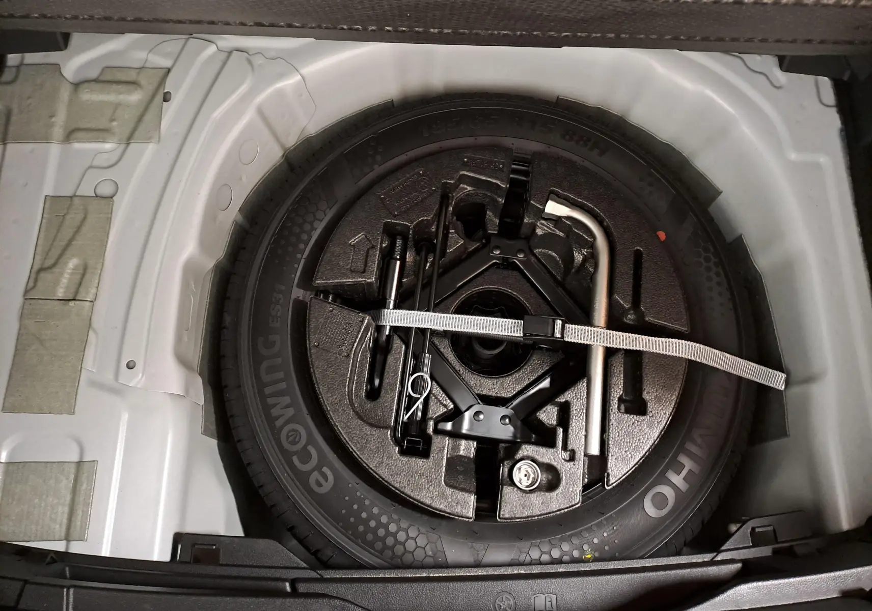 Vue plongeante sur la roue de secours et les outils de bord dans le coffre d’une Volkswagen Polo blanche 2024.