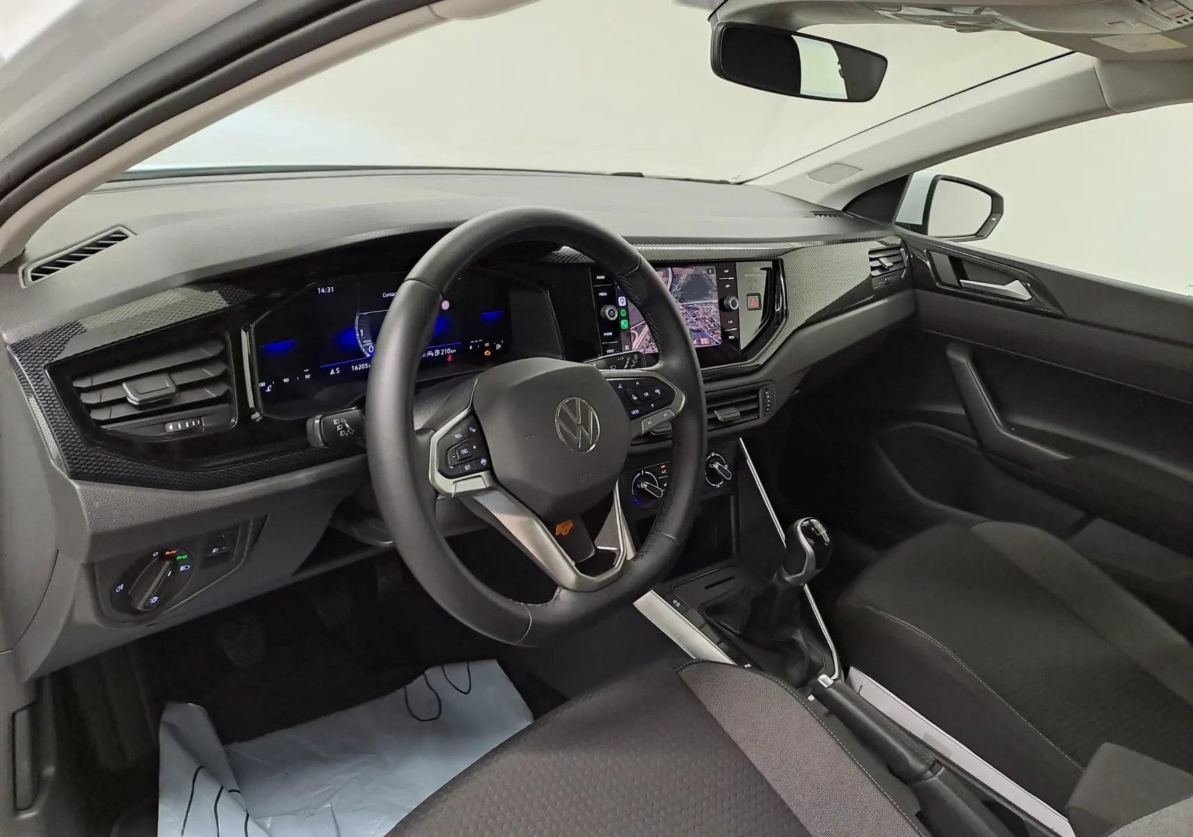 Vue intérieure côté conducteur de la Volkswagen Polo 2024 blanche, avec tableau de bord numérique et boîte manuelle visible.