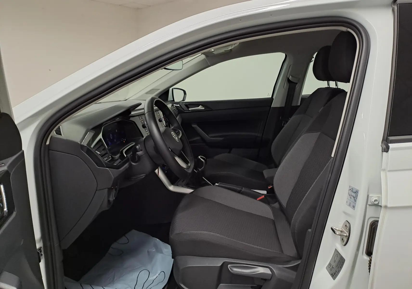 Vue intérieure côté conducteur d'une Volkswagen Polo blanc pur 2024, montrant les sièges avant et le tableau de bord.