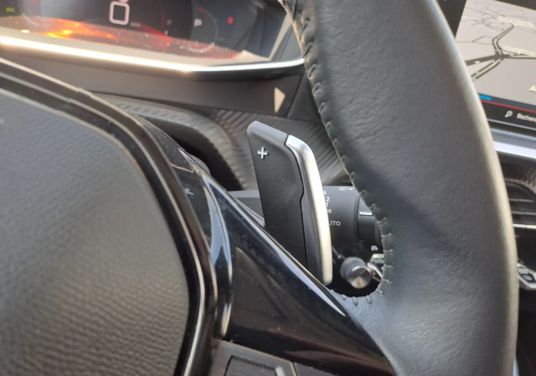 Gros plan sur la palette de changement de vitesse droite du volant noir du Peugeot 2008 rouge, tableau de bord en arrière-plan.