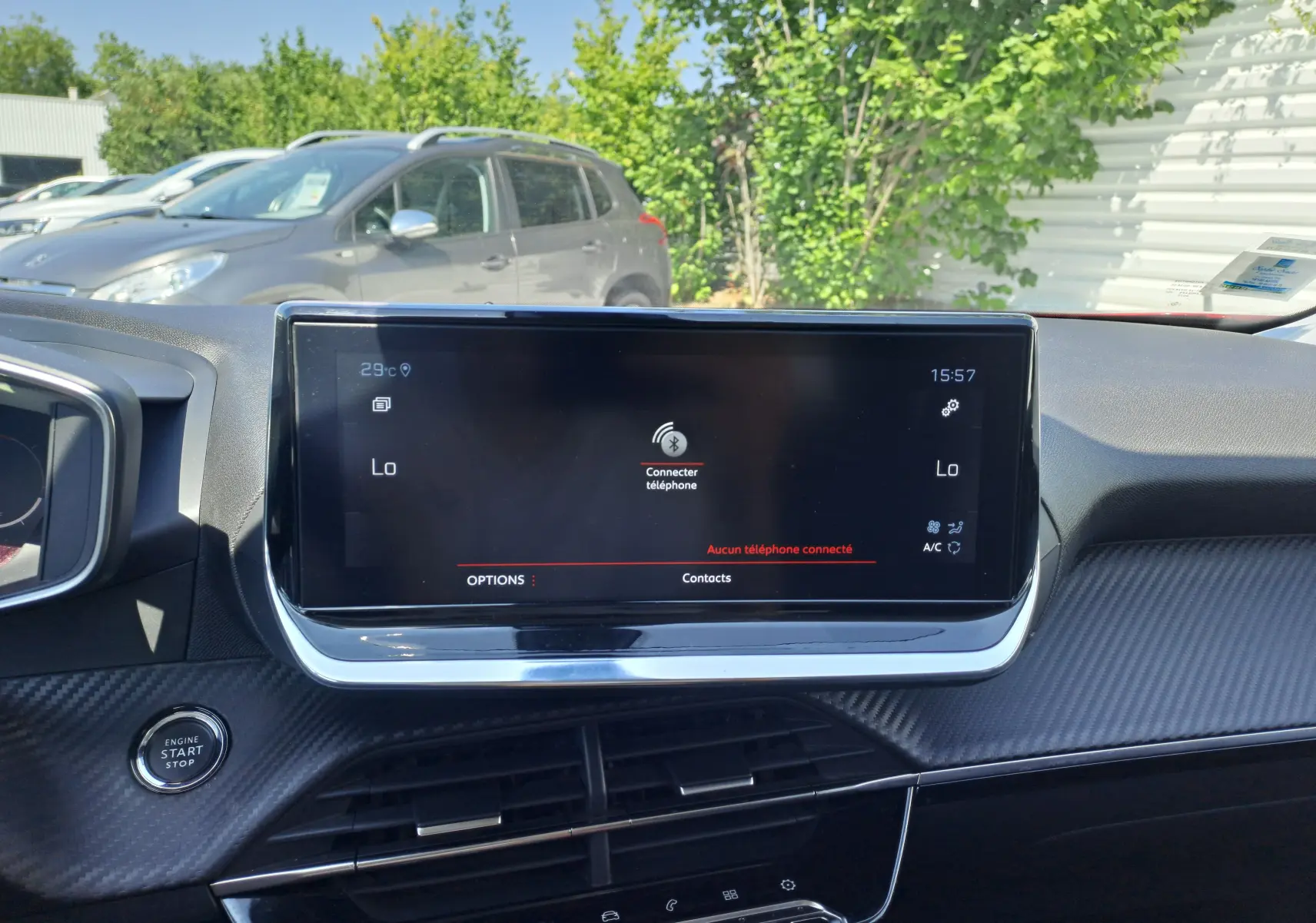 Écran tactile central du tableau de bord du Peugeot 2008 rouge, avec bouton start/stop et finition carbone visible.