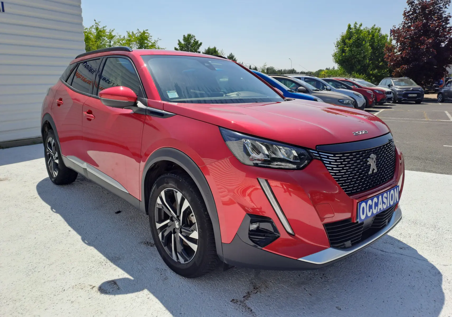 Peugeot 2008 rouge vue 3/4 avant droit, avec calandre noire et feux LED distinctifs, stationnée en extérieur.