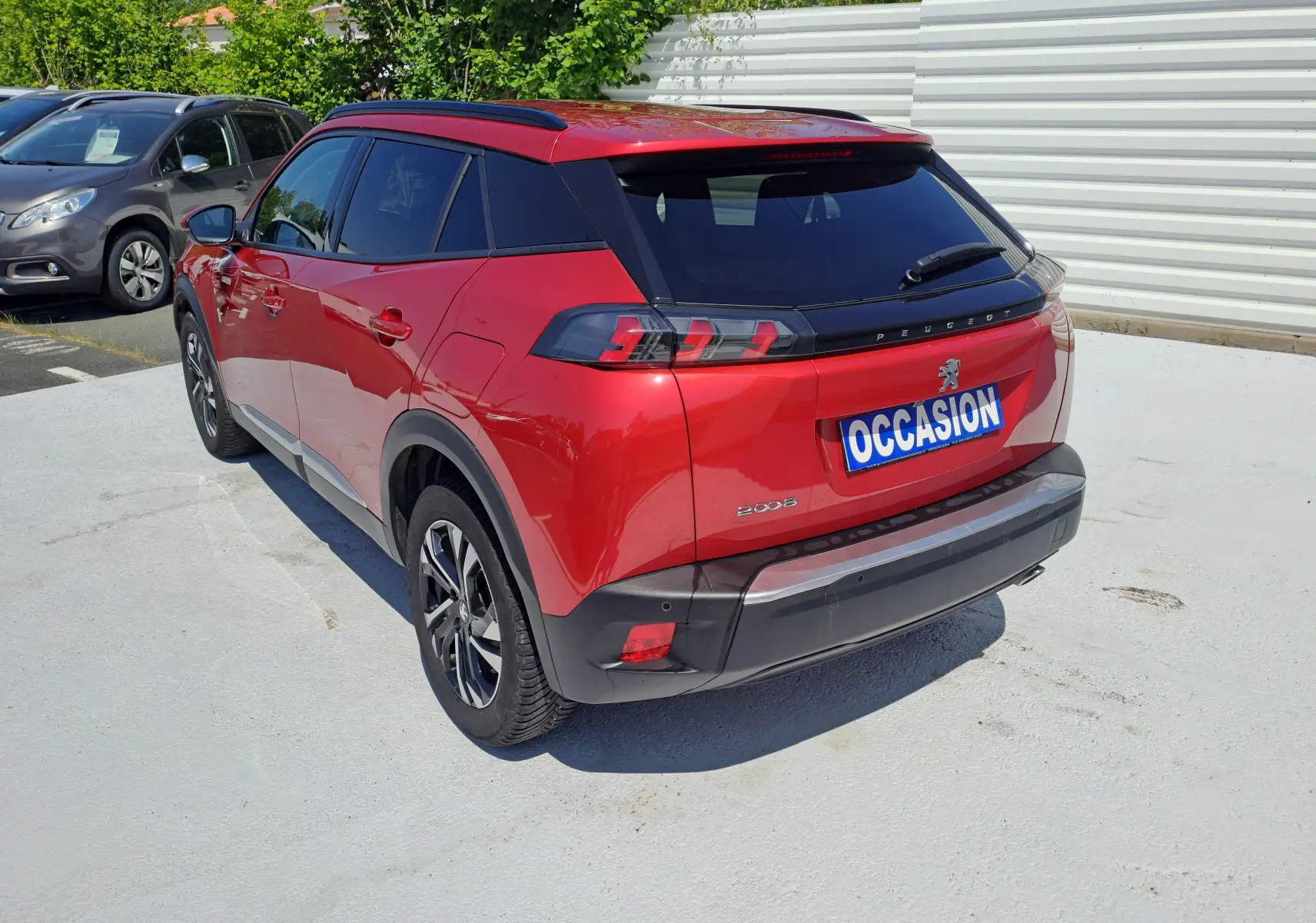 Peugeot 2008 rouge vue en 3/4 arrière droit, avec feux arrière LED et toit noir brillant sur parking.