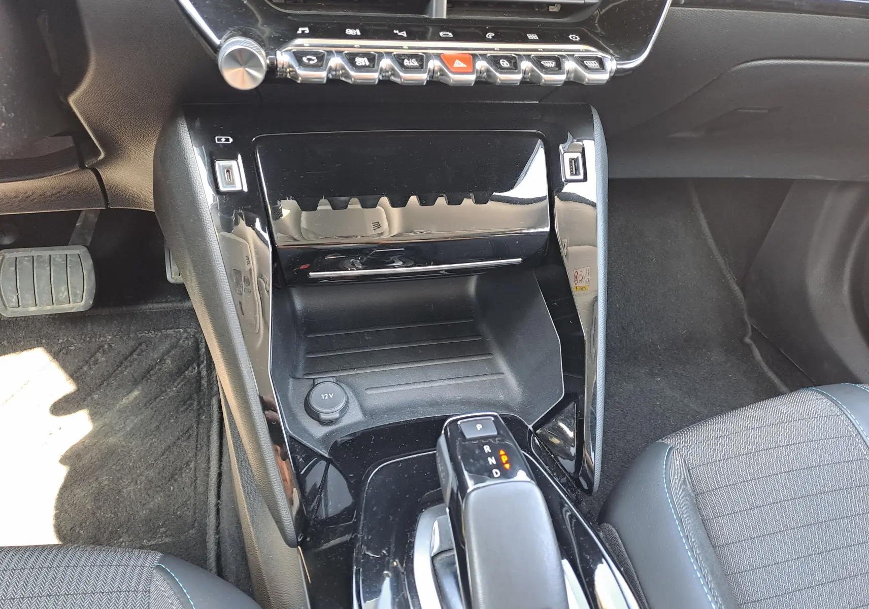 Vue rapprochée de la console centrale noire brillante du Peugeot 2008 rouge, avec levier de boîte auto et commandes tactiles.