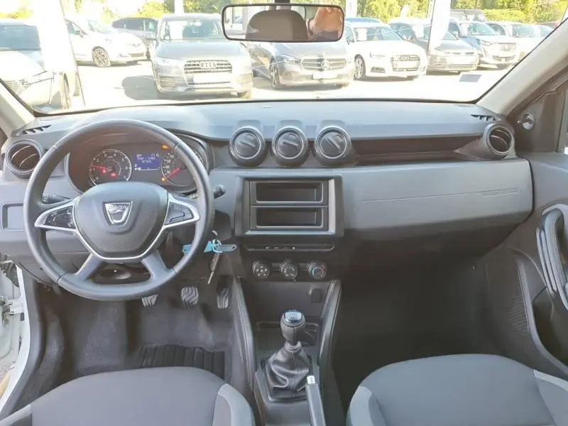 Intérieur du Dacia Duster blanc 2021, vue frontale du tableau de bord avec volant, commandes et boîte manuelle visible.
