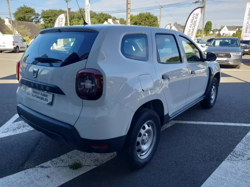 Vue 3/4 arrière droite d'un Dacia Duster blanc Glacier 2021 avec roues acier et feux arrière sombres.