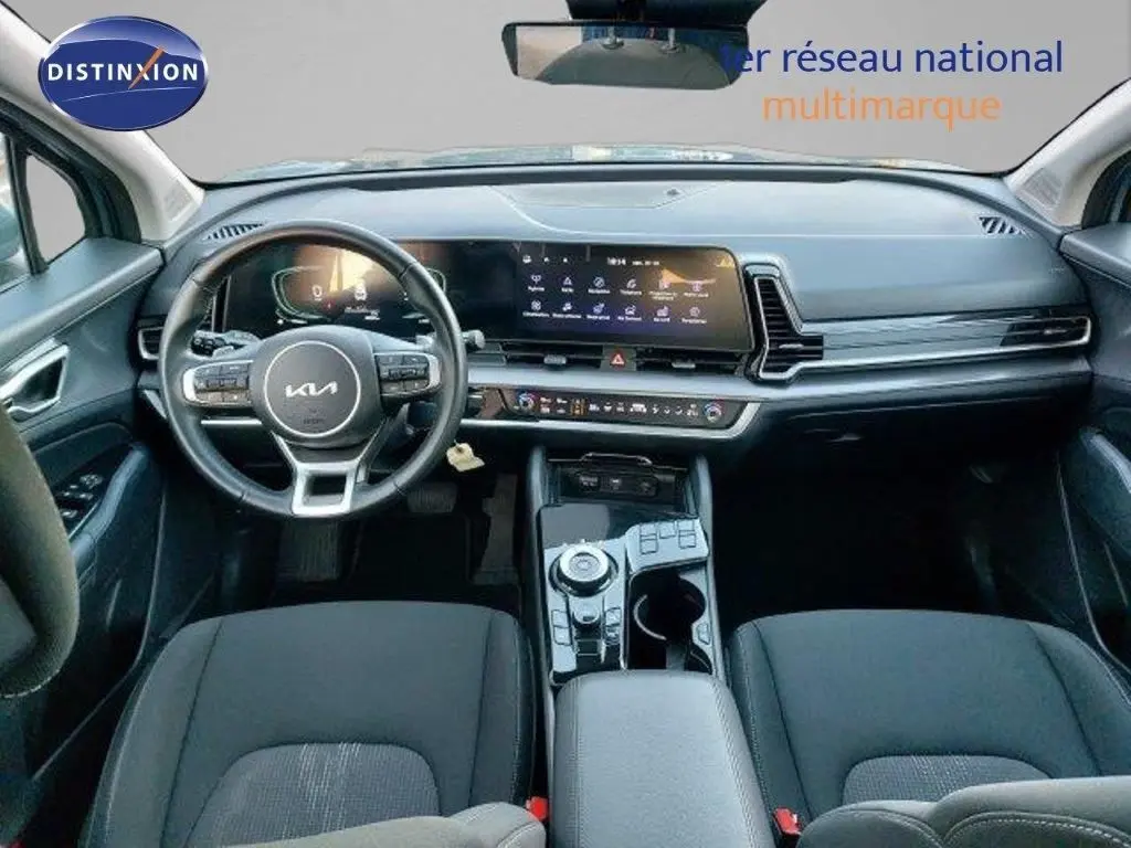 Vue intérieure avant du tableau de bord du Kia Sportage 2024 avec écran tactile large et volant multifonction noir.