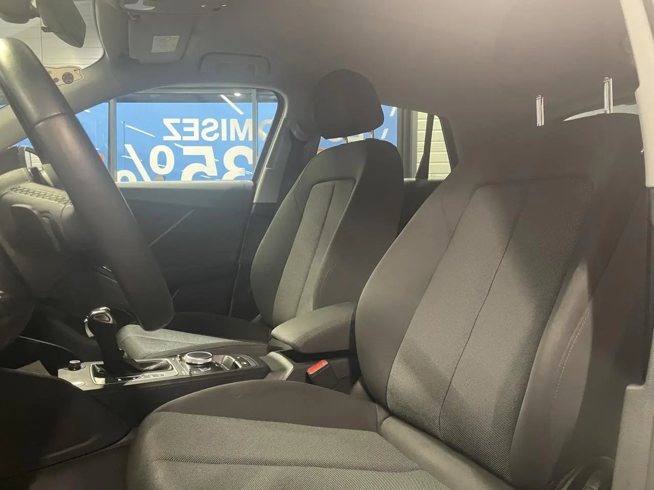 Vue intérieure côté droit montrant les sièges avant en tissu noir et la console centrale d’un Audi Q2 noir métallisé.