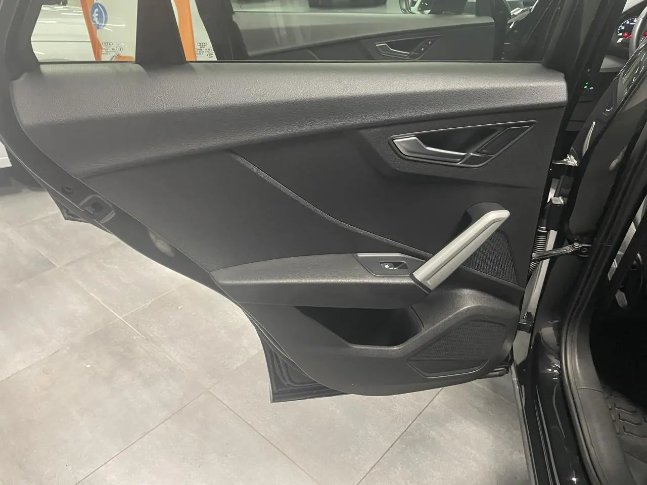 Vue intérieure de la porte arrière gauche noire métallisée de l'Audi Q2 2023 avec poignée et commandes en aluminium.