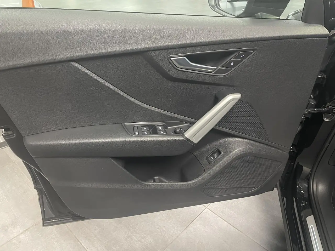 Porte avant gauche ouverte d’Audi Q2 noir métallisé 2023, avec poignée aluminium et commandes électriques.