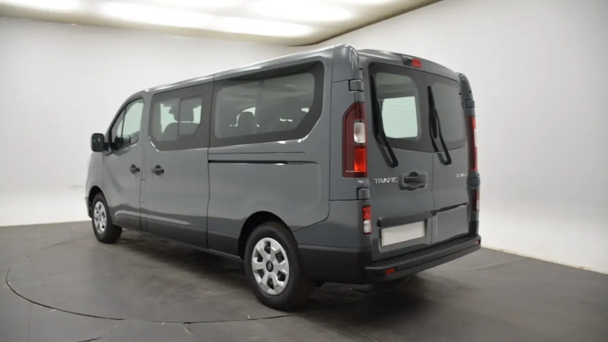 Renault Trafic Fourgon gris clair vu en 3/4 arrière droit, avec vitres latérales et portes arrière battantes.