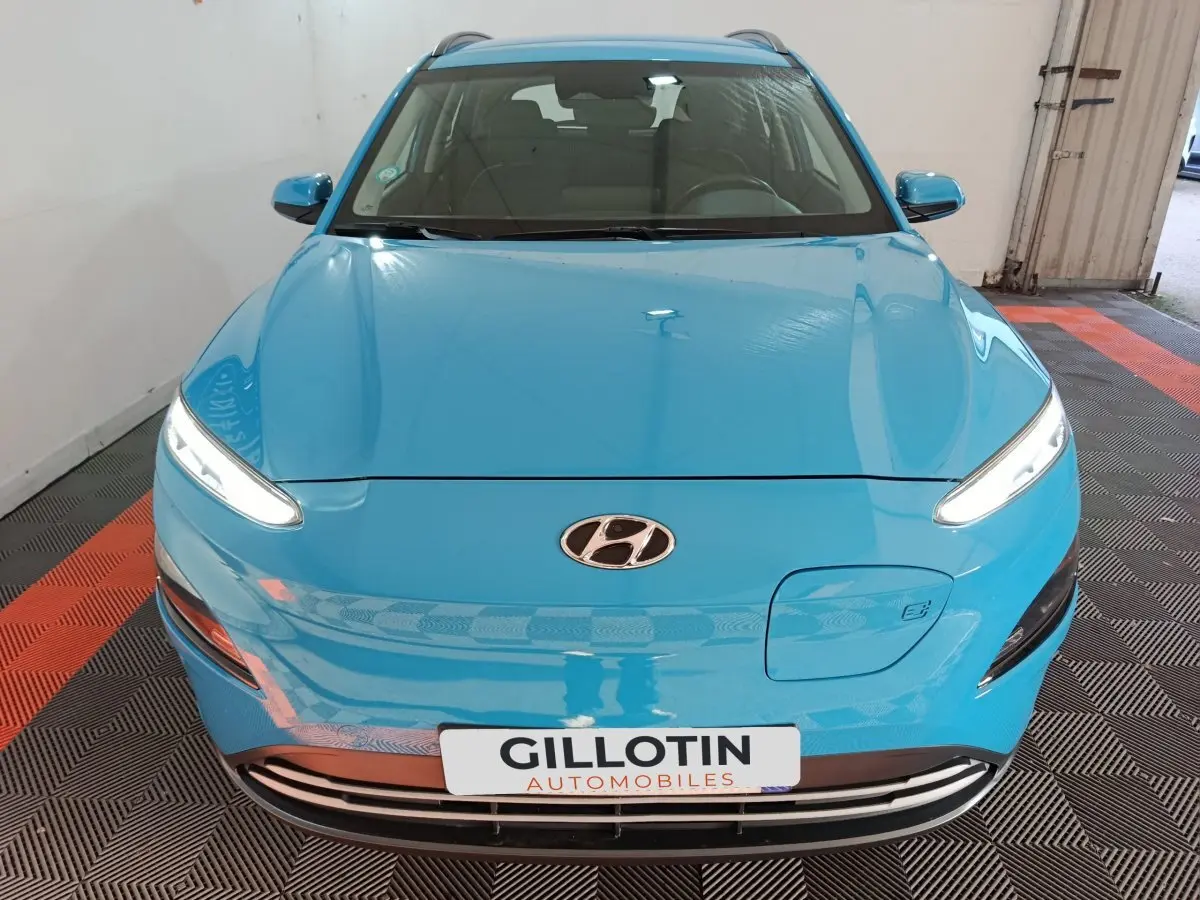 Vue avant d’un Hyundai Kona électrique bleu avec phares LED allumés et logo Hyundai visible sur le capot.
