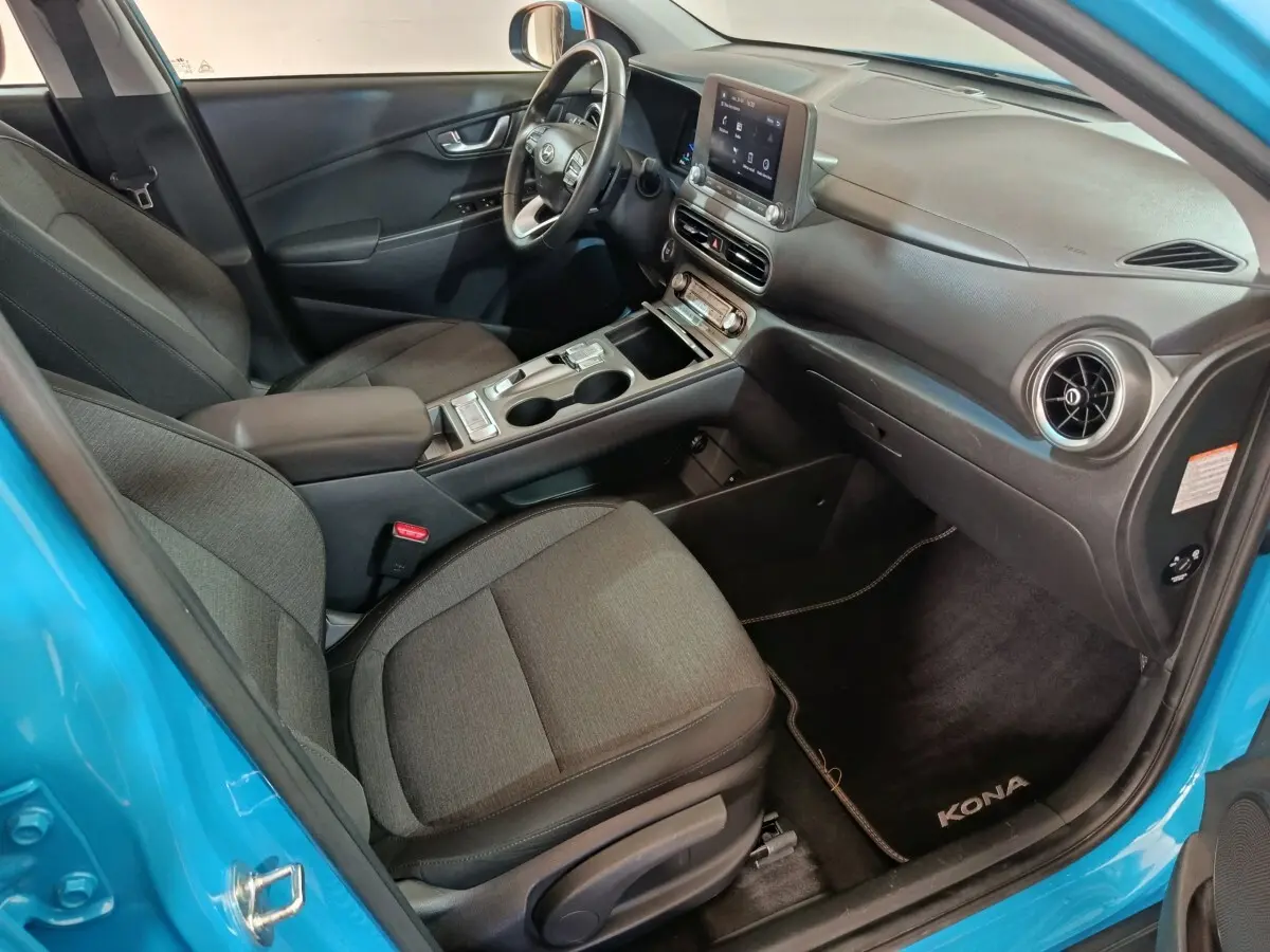 Vue intérieure côté passager du Hyundai Kona bleu 2022, avec tableau de bord central tactile et sièges tissu gris.