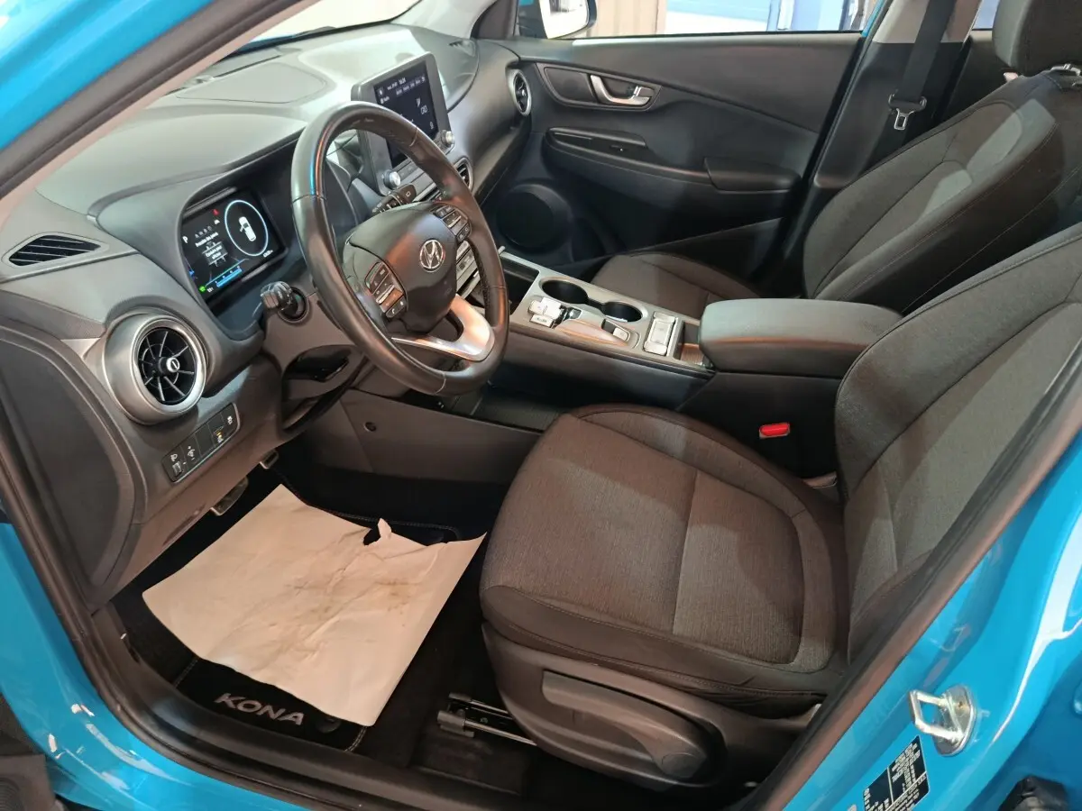 Vue intérieure côté conducteur du Hyundai Kona bleu 2022, avec tableau de bord digital et volant cuir multifonctions.