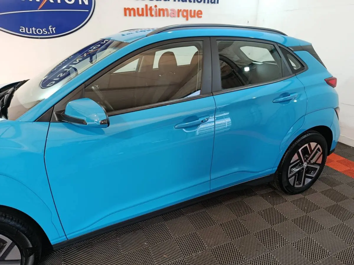 Vue latérale côté gauche d'un Hyundai Kona électrique bleu 2022 avec jantes distinctives et rétroviseur assorti.