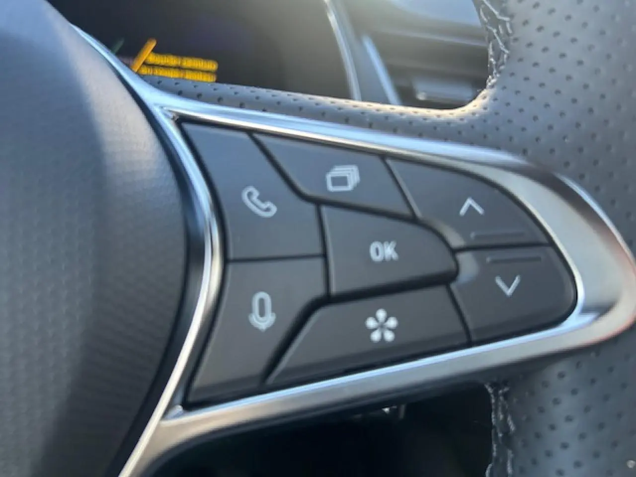 Gros plan sur les commandes multifonctions noires et argentées du volant perforé du Renault Symbioz blanc nacré.