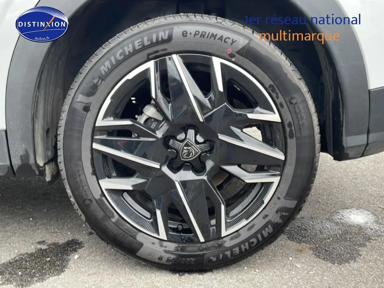 Gros plan sur la roue avant gauche d’un Peugeot 3008 blanc, jante alu noire et argent avec logo lion central.